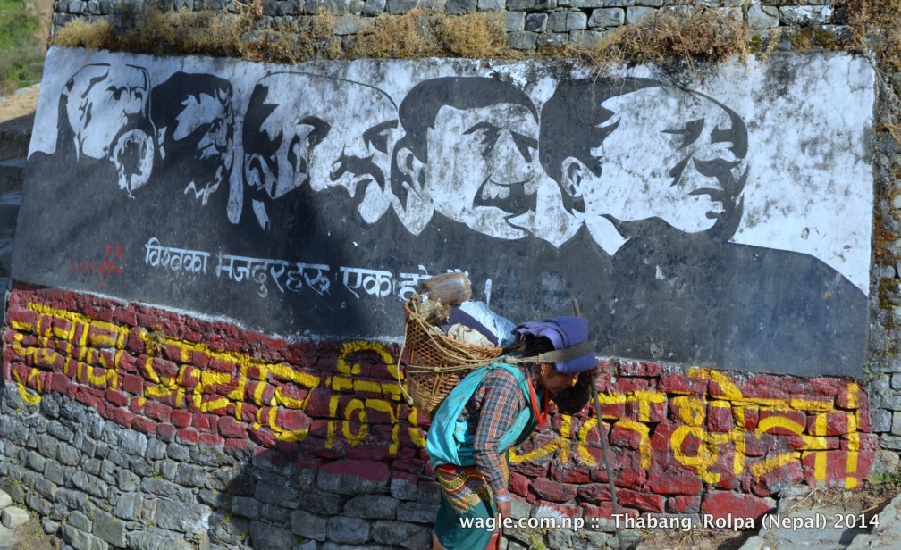 A woman walks past a Maoist mural at the entrance of Thabang village, Rolpa: 1st line: Workers of the world, unite. 2nd line: No election campaign zone!