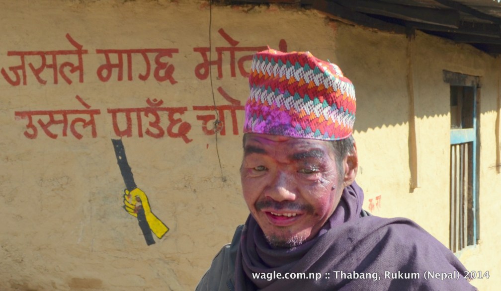 A man in Thabang, Rolpa, face smeared with colored powder, celebrated Maghi festival. On the background is an anti-election slogan- 